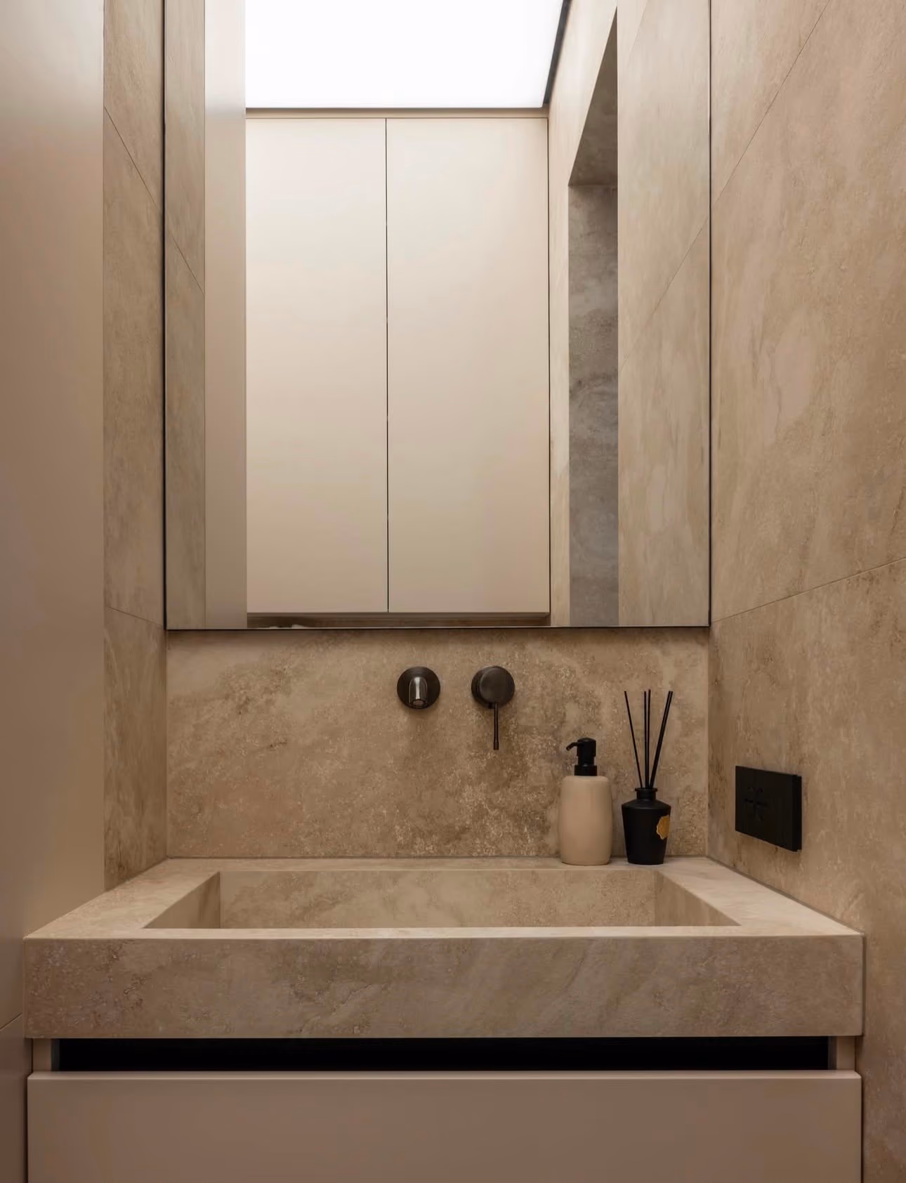 Gaeste-WC mit Waschtisch und Wandflaechen in heller Travertinoptik und Spiegelschrank.