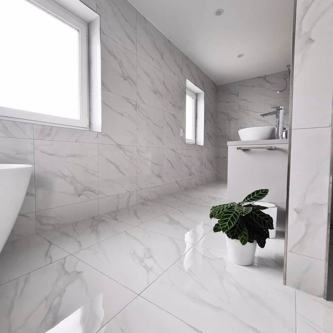 Helles Badezimmer mit weissen, marmorierten Wand- und Bodenfliesen, freistehender Wanne und Waschtisch.